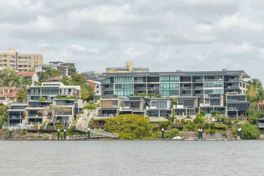 Modern riverside apartment buildings with lush greenery.