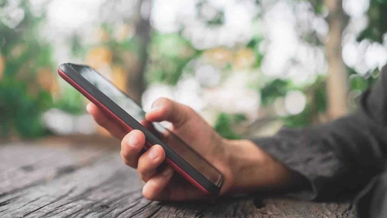 Hand holding smartphone outdoors on wooden surface
