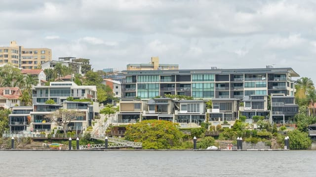 Modern riverside apartment buildings with lush greenery.