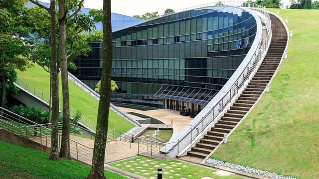Modern building with curved design on green hill.