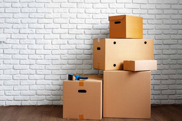 Stacked cardboard boxes against white brick wall.