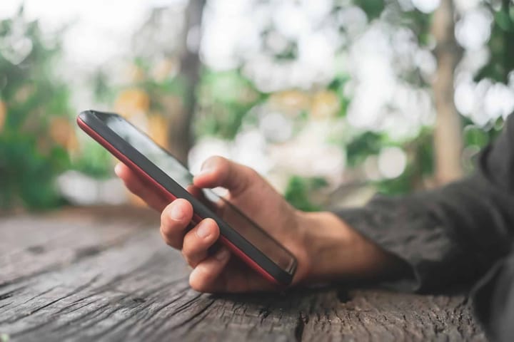 Hand holding smartphone outdoors on wooden surface