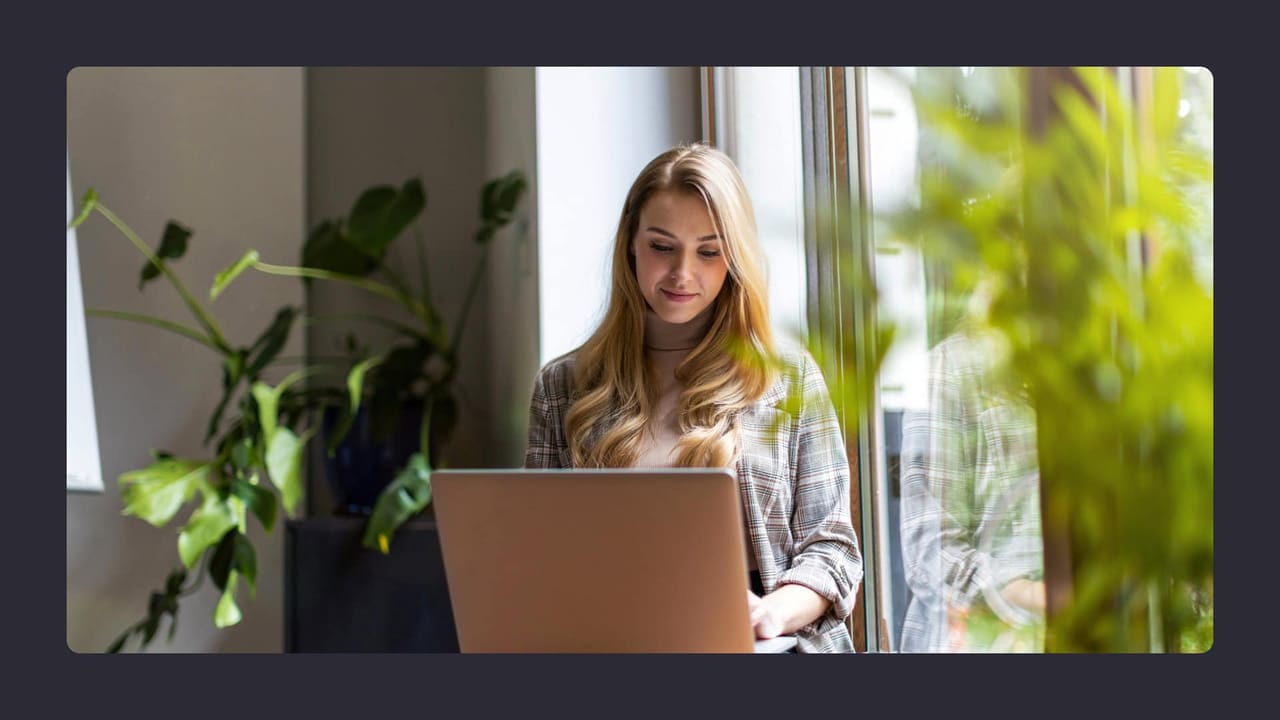 Woman working on laptop near window with plants