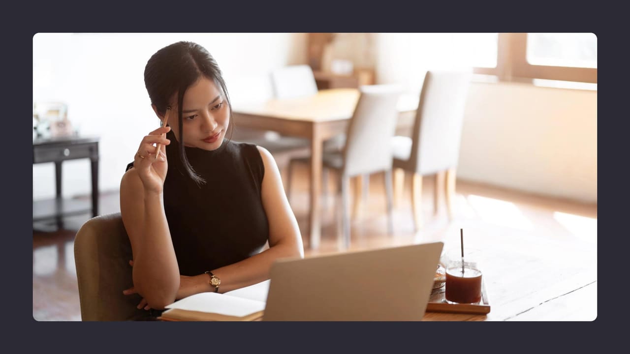 Woman pondering while working on laptop in café