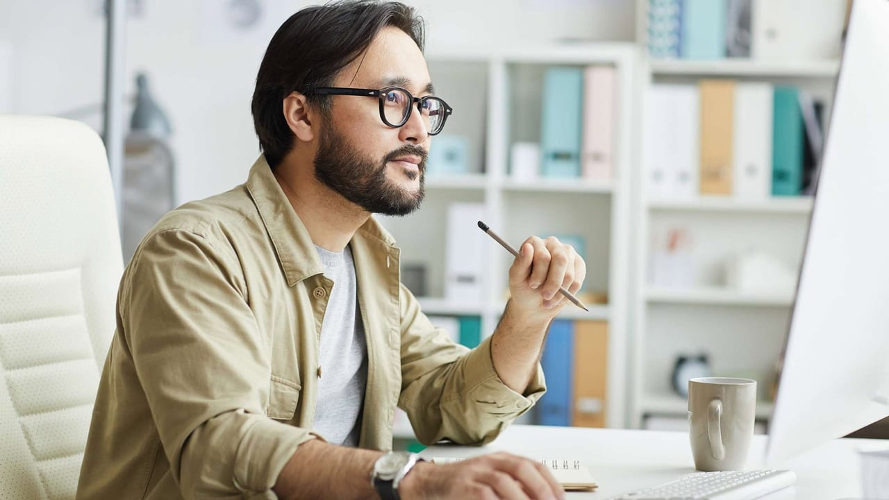 Man pondering at desk with computer, office background