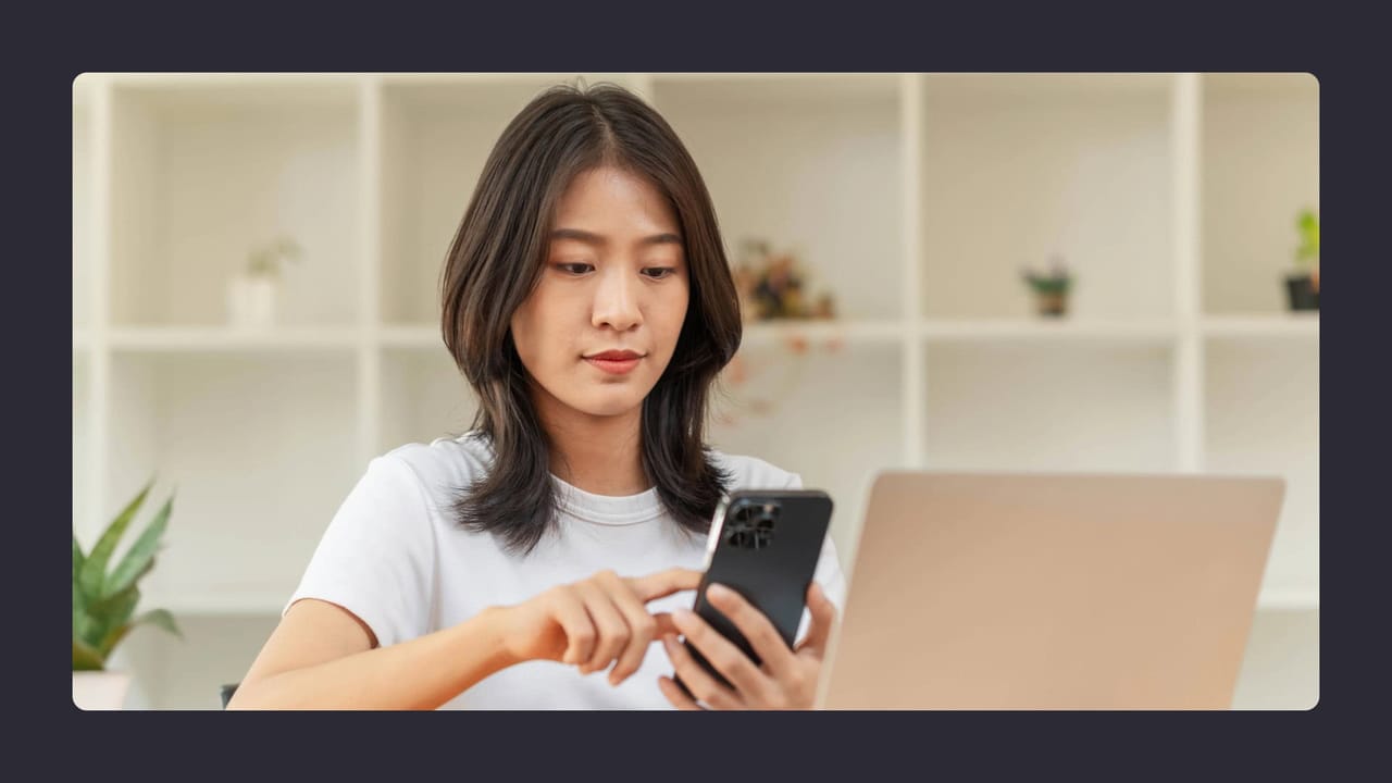 Woman using smartphone near laptop in office