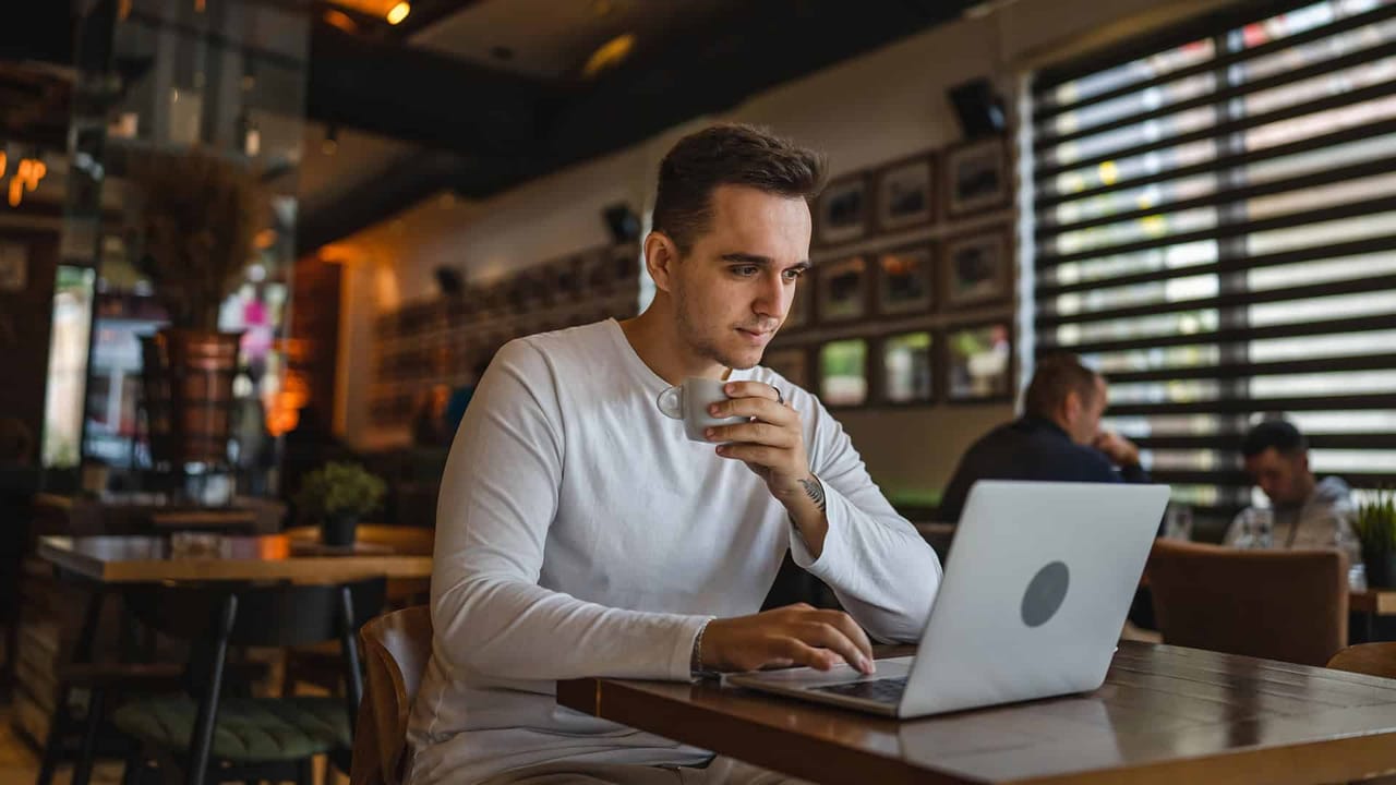 Man drinking coffee and using laptop in café.