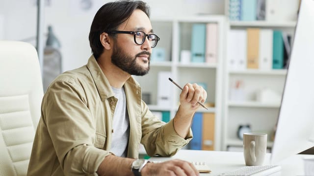 Man pondering at desk with computer, office background