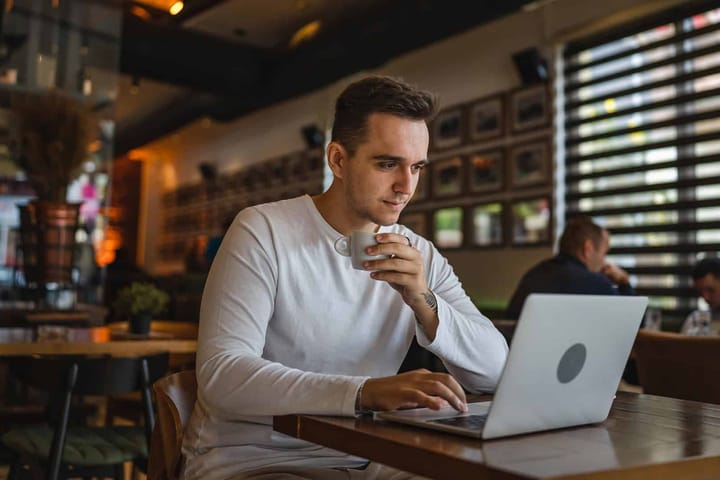 Man drinking coffee and using laptop in café.