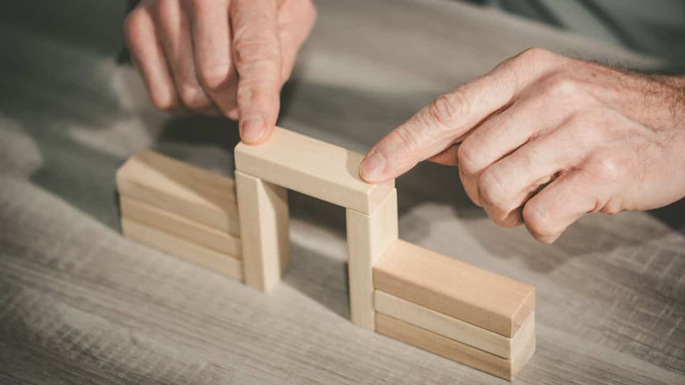 Hands building arch with wooden blocks on table.