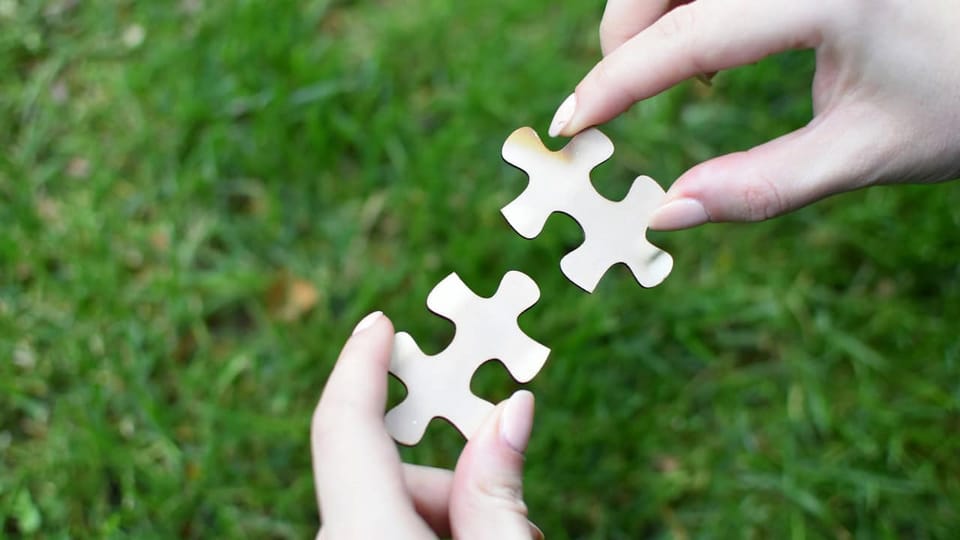 Hands connecting puzzle pieces on grass