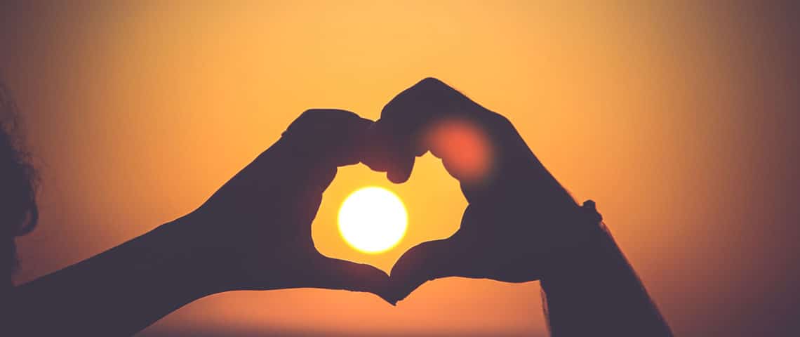 Human hands form a heart silhouette cast against sunset light