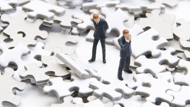 2 figurine men searching for something on the puzzle pieces
