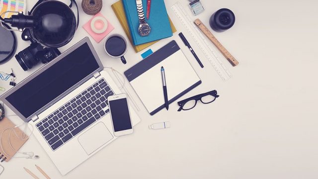 A photograph of a desk filled with items such as laptop, mobile phone, tablet, notebook, camera and headphones to help build your business
