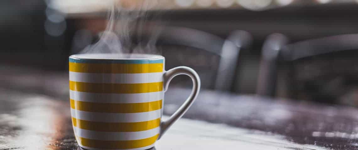 Steaming coffee mug with yellow stripes on top of table