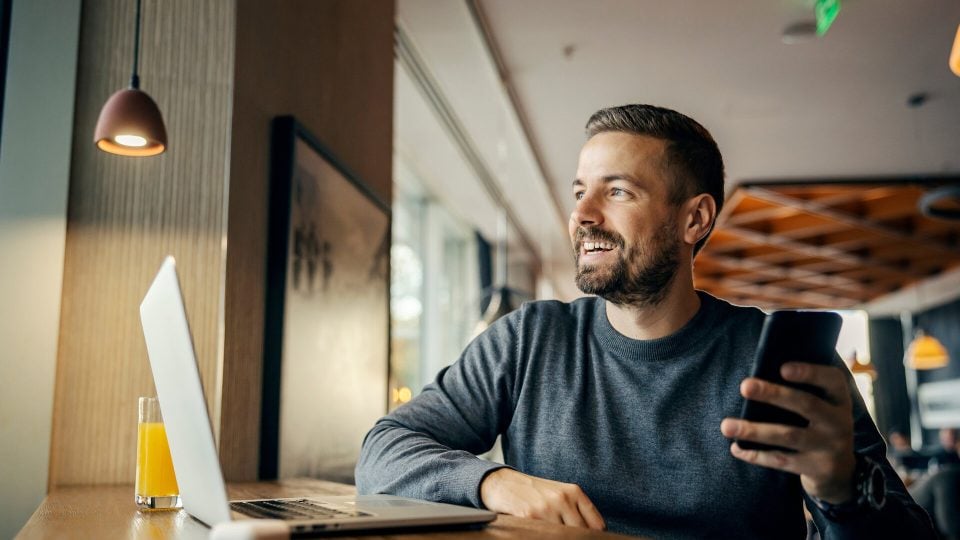 An entrepreneur sitting in a coffee shop happy knowing that his business website maintenance plan is working effectively.