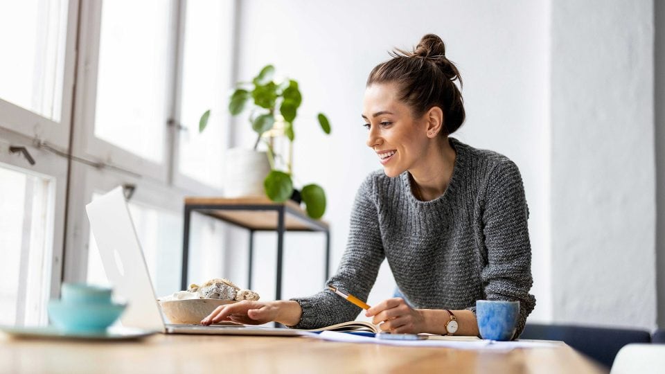 A happy young woman browsing a secure website on her laptop in her home studio.
