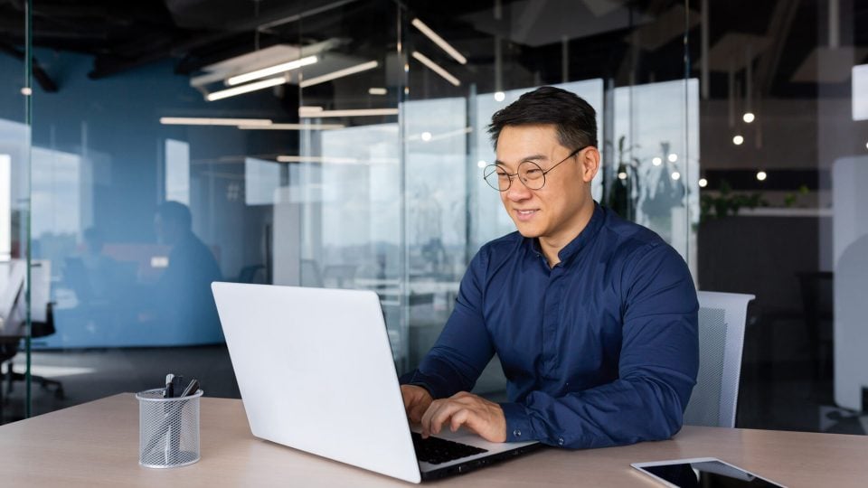 Successful mature asian man wearing glasses working on a laptop