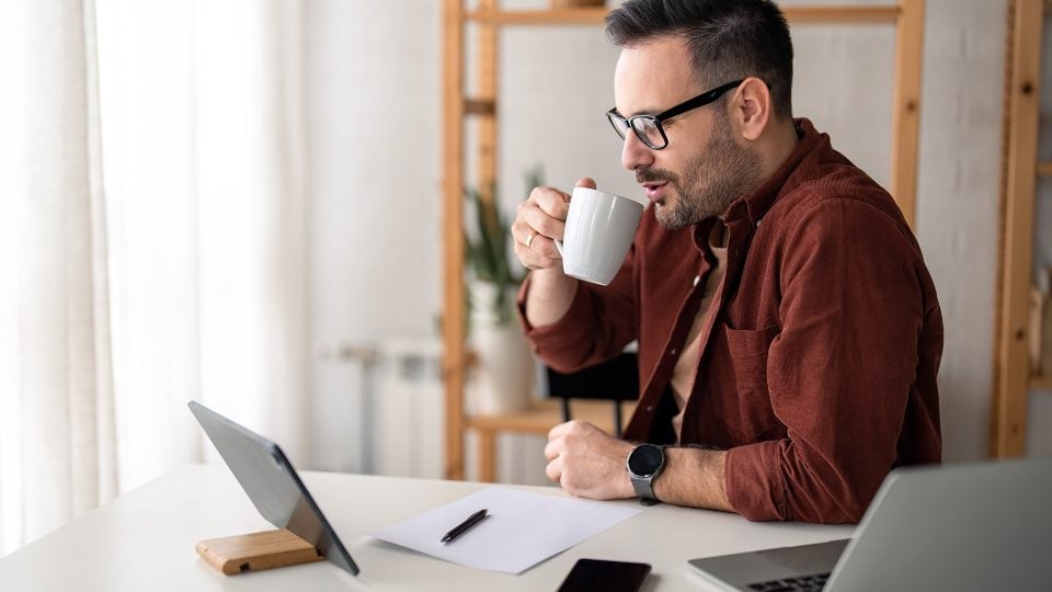 Man having coffee while using multiple digital devices a laptop and tablet