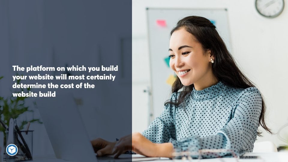 Smiling asian businesswoman sitting at desk and using laptop in office deciding what platform to use to build her website.