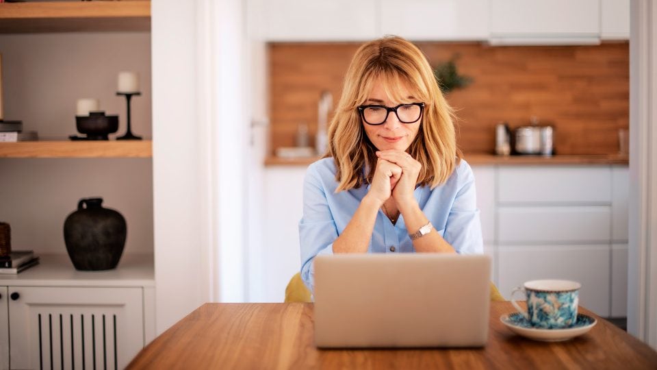 Middle aged woman sitting at a table and using her laptop to contact Chillybin for website maintenance services.