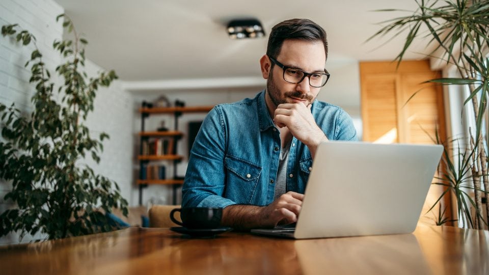 Portrait of a man using a laptop at home to investigate the cost of website maintenance.