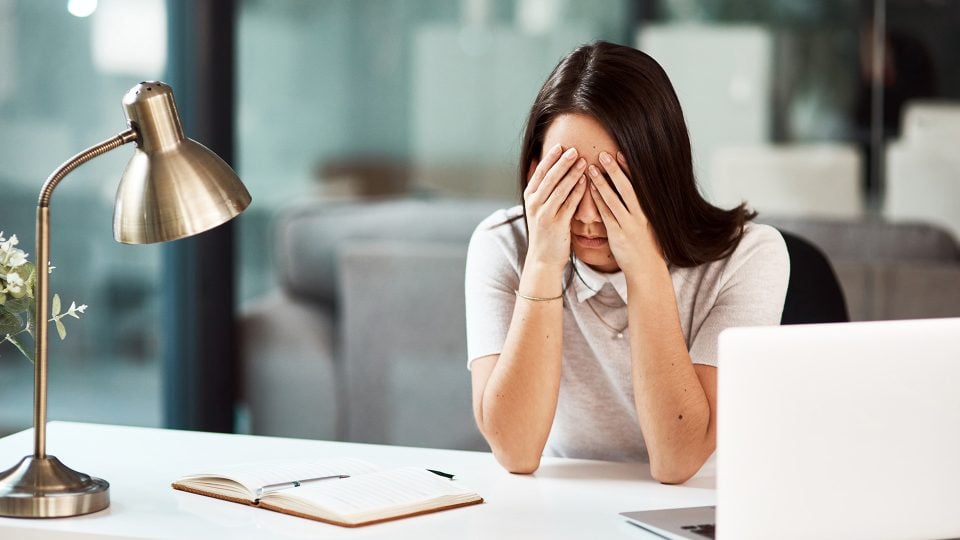 Young businesswoman sitting at her desk with her hands over her eyes looking stressed out because she did not plan her web design project effectively.