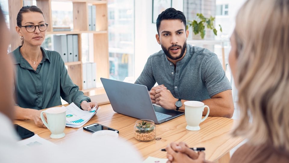 Diverse team in a meeting discussing the limitations of using platforms like Squarespace, with a woman presenting a business strategy to a CEO and colleagues in an office setting.