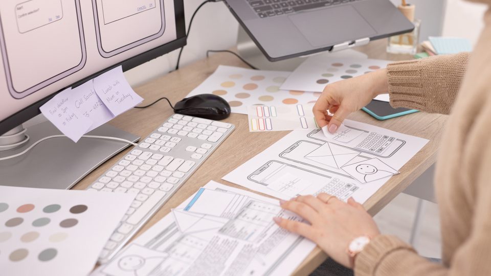 Woman meticulously planning UX design for a mobile app, highlighting graphic design, software development, and UI strategy on a multimedia tech setup.