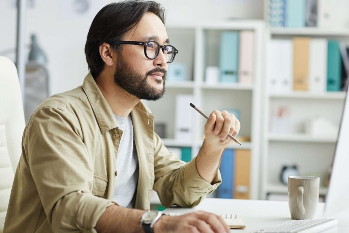 Man pondering at desk with computer, office background