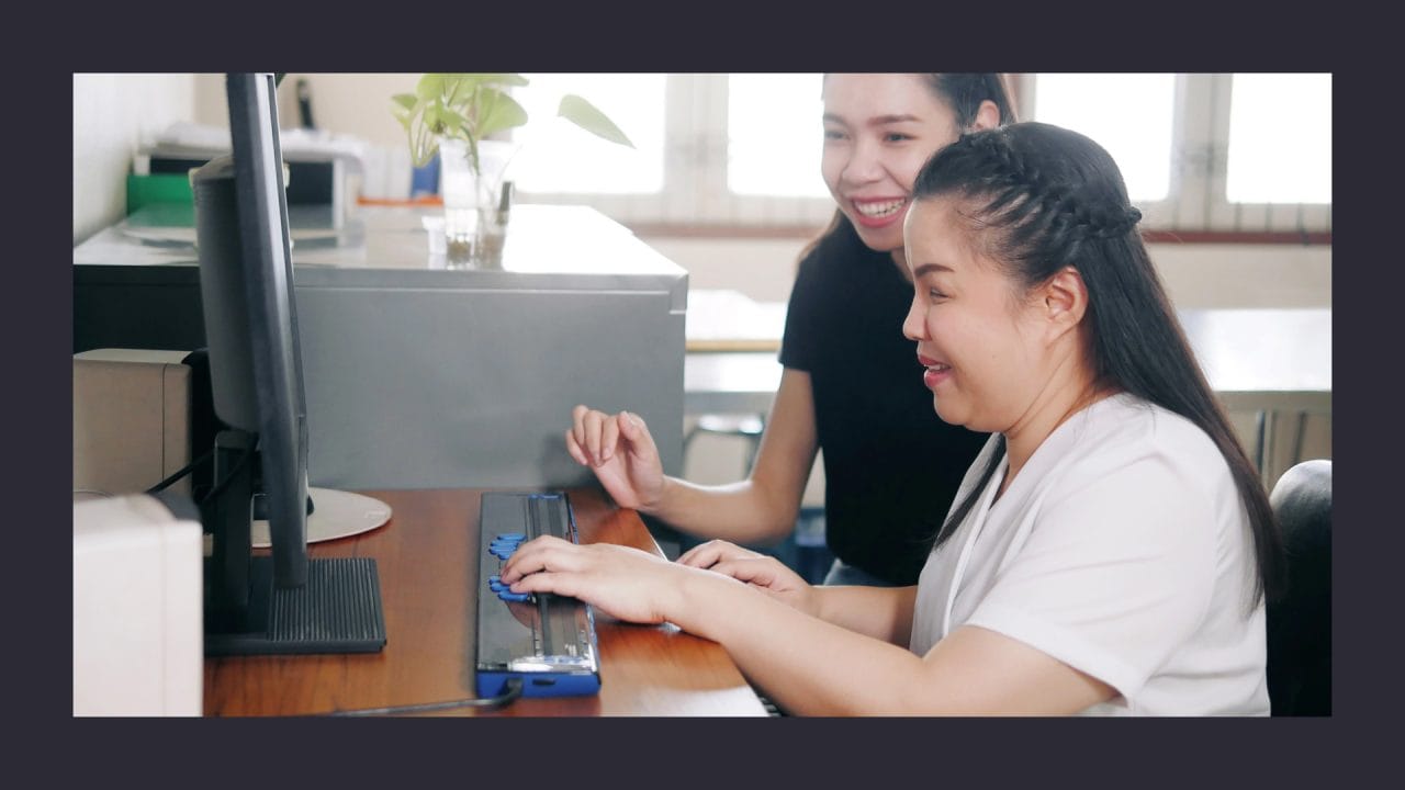 Two women smiling and working on computer in office