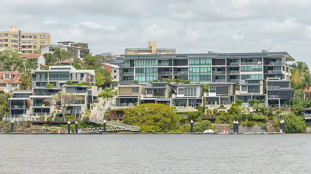 Modern riverside apartment buildings with lush greenery.