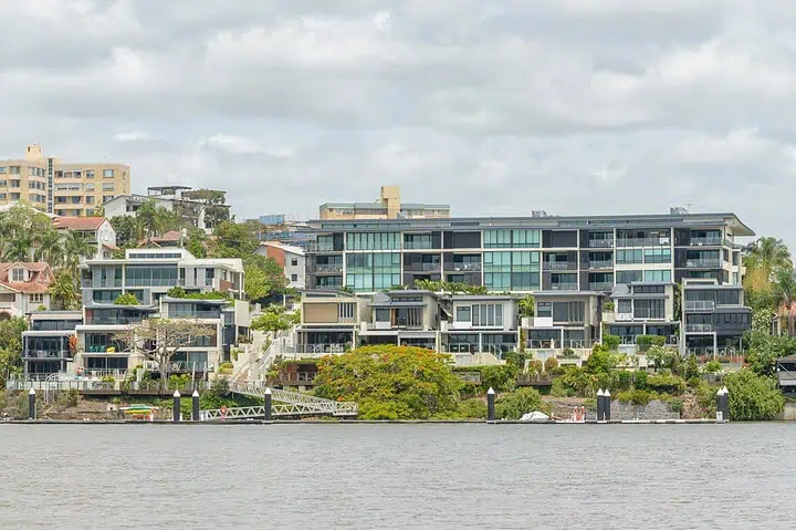 Modern riverside apartment buildings with lush greenery.