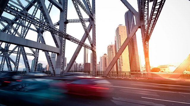 Traffic crossing bridge with city skyline at sunset.