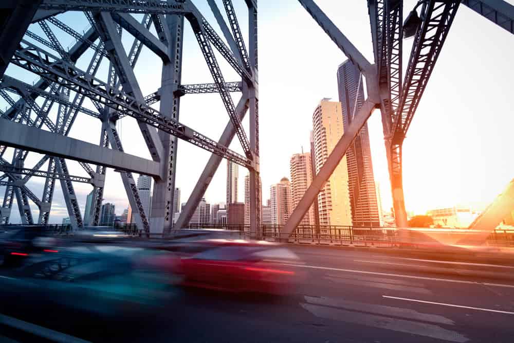 Traffic crossing bridge with city skyline at sunset.