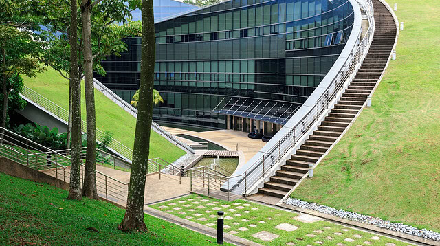 Modern building with curved design on green hill.
